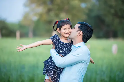 A man holding his daughter in the grass.